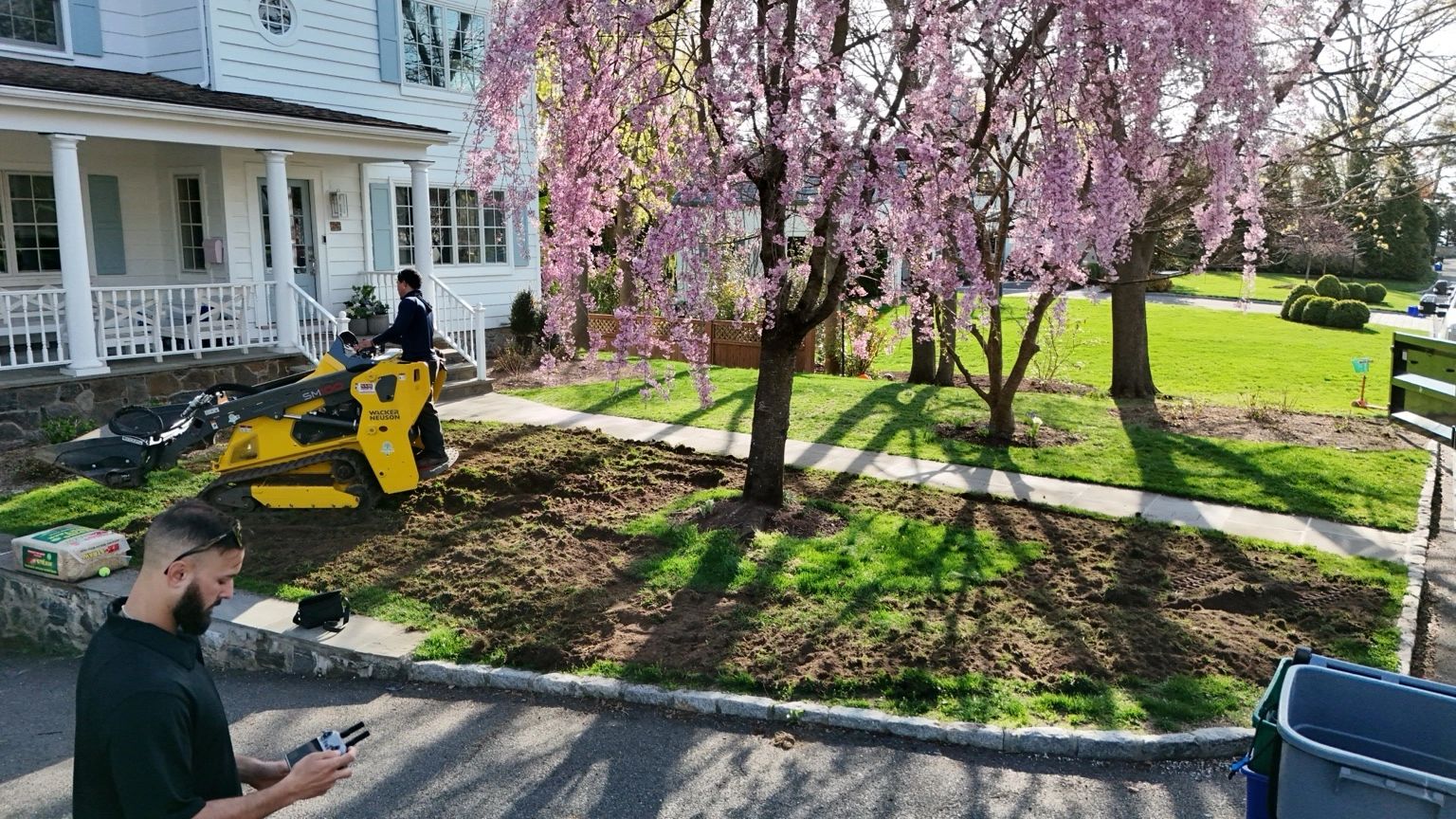 Aerial photo of front yard lawn preparation in Rye, New York with a compact machine reworking the soil around mature trees and walkway areas before new sod installation.