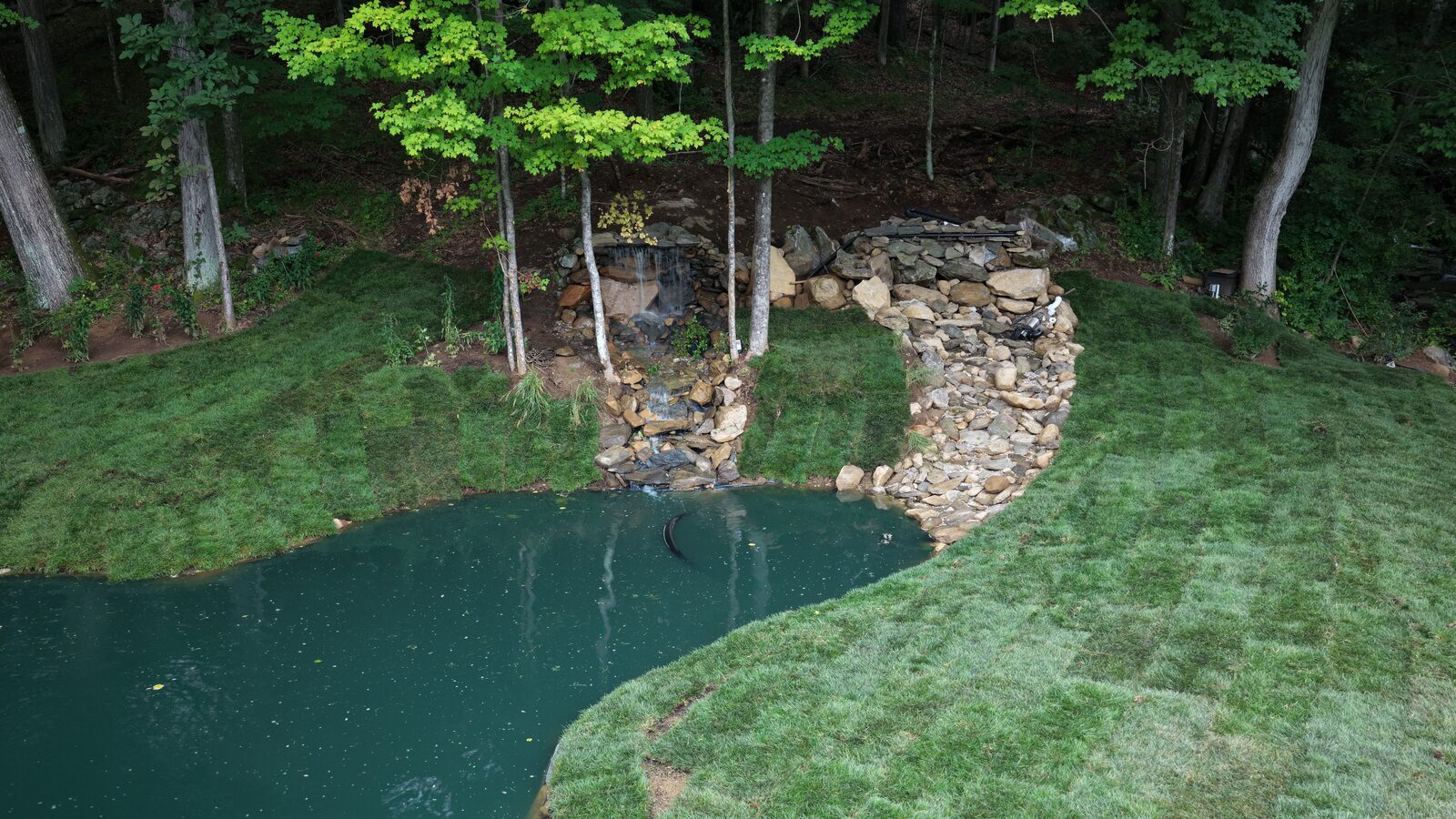 Aerial view of fresh tall fescue sod meeting the stone waterfall edge at a Bridgewater pond landscape