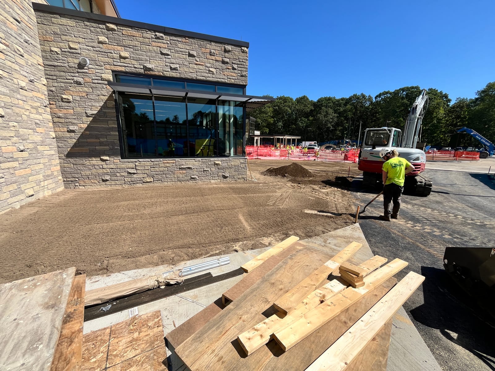 Pre-install grading beside the new Central Middle School building in Greenwich, CT with an excavator and site crew preparing soil near finished stone and glass walls