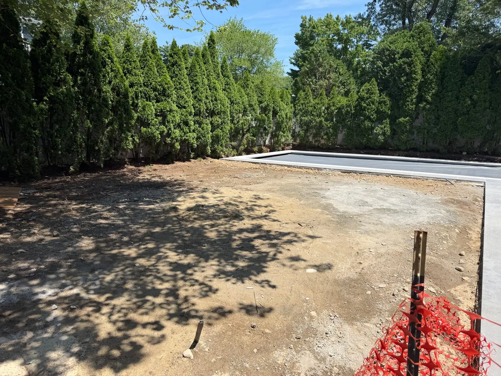 Bare, debris-filled rough grade beside the new pool deck after a pool build in Fairfield, CT