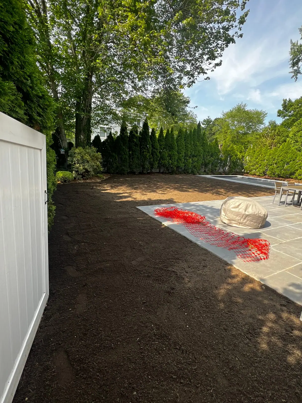 Fresh screened topsoil fine-graded across a Fairfield, CT backyard after pool-build debris removal, with the new pool and stone patio beyond