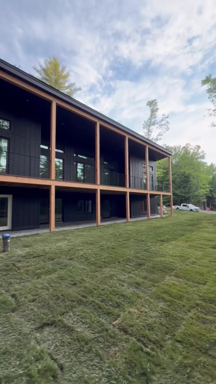 The finished tall fescue lawn running along the side of the modern home, the Vermont tree line mirrored in the glass