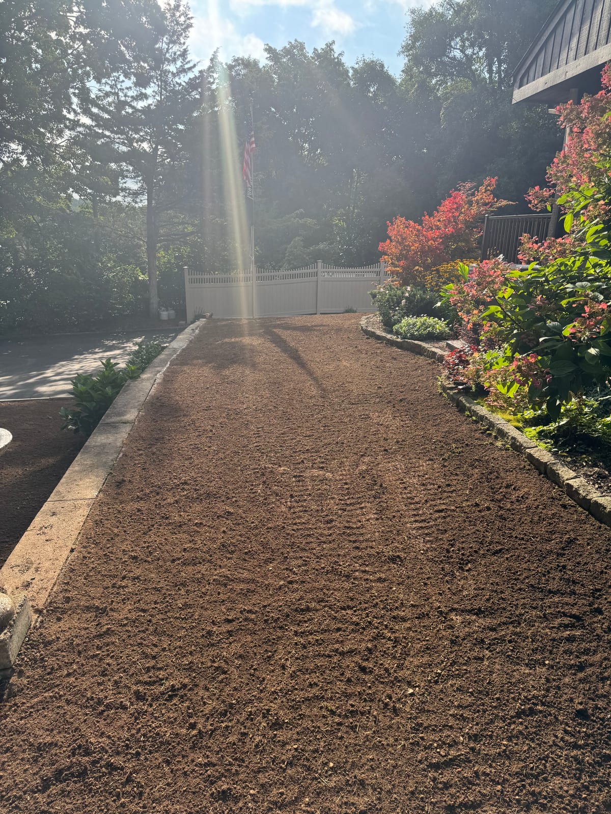 Graded bare soil run beside the driveway of a Meriden, CT home in early morning light, prepped and awaiting sod delivery