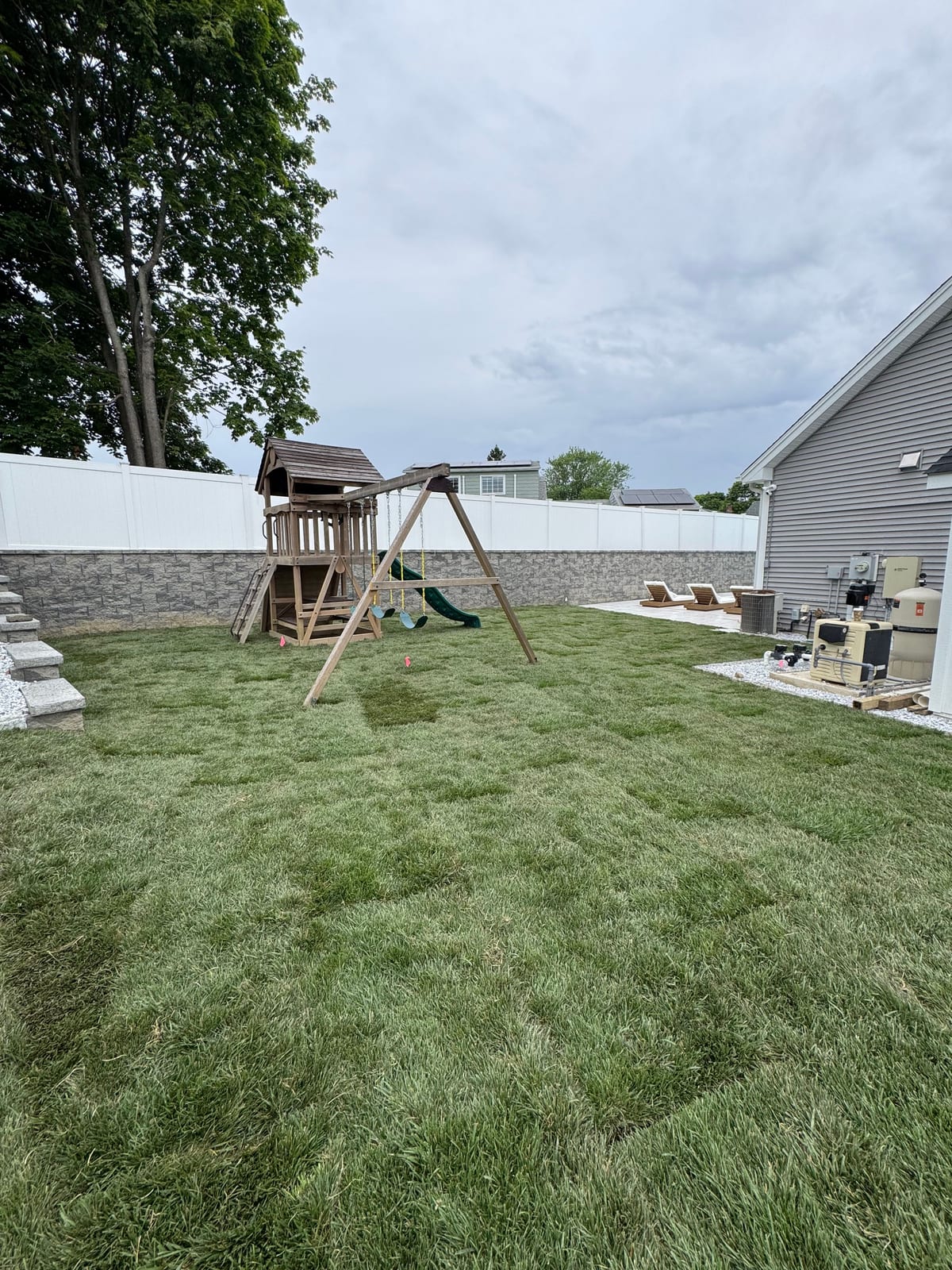 Finished tall fescue backyard lawn around a playset in Milford, CT, bordered by a white privacy fence with the pool patio along the house
