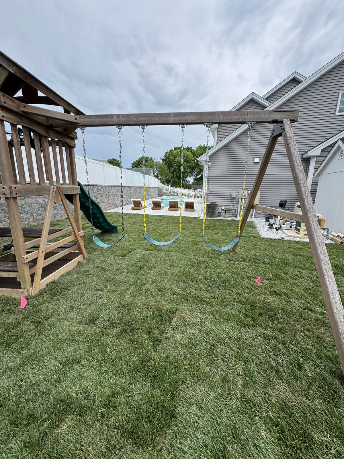 Fresh tall fescue sod under the backyard swing set in Milford, CT, with the in-ground pool, lounge chairs, and patio just beyond and the white privacy fence wrapping the yard