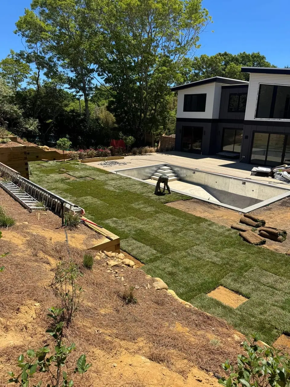CT Sod crew laying fresh sod around the pool during a 3,000 sq ft installation in Montauk, NY, with sod rolls staged on the new lawn