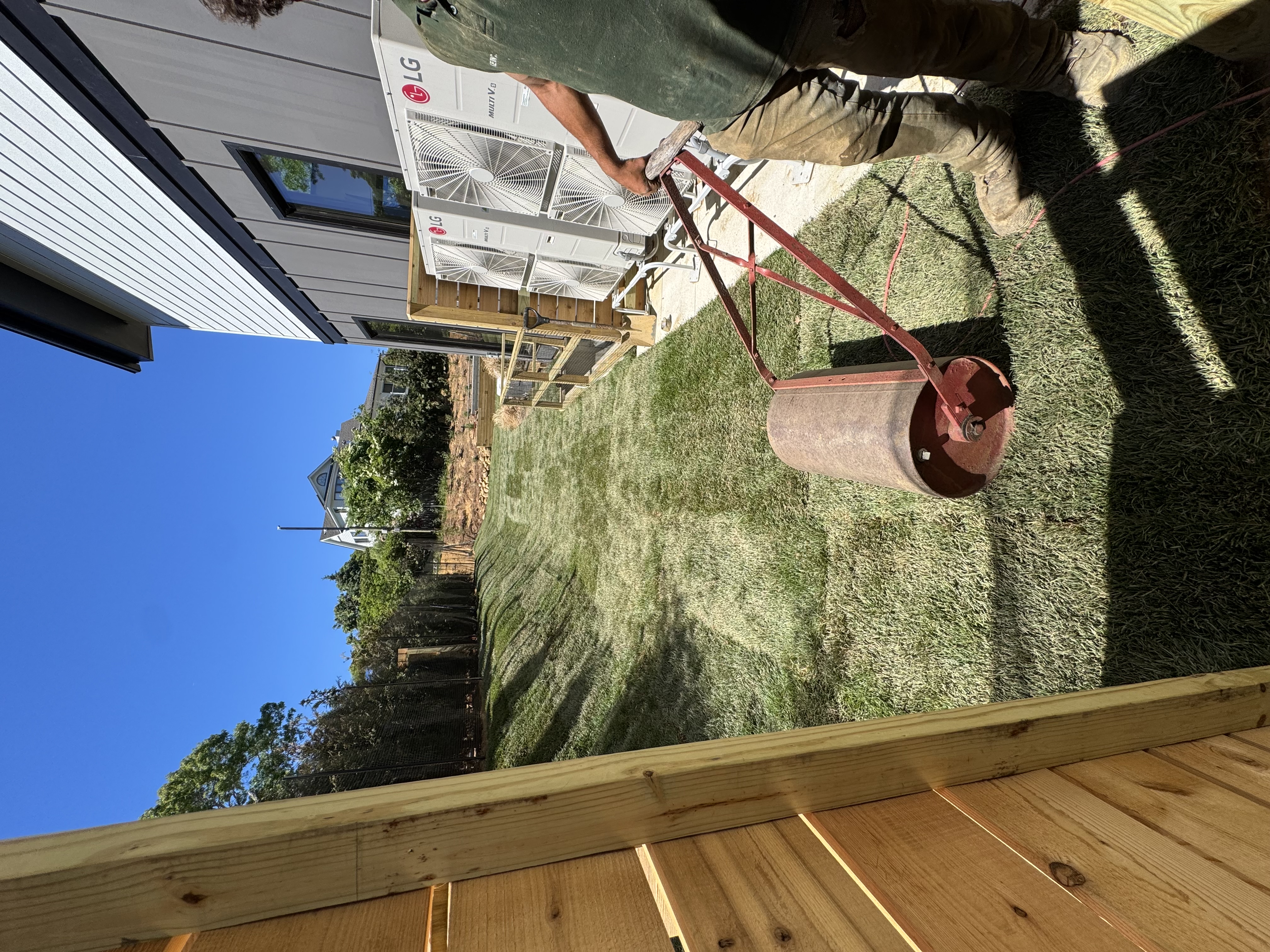 CT Sod installer using a lawn roller to press down freshly laid sod in the side yard during a sod installation in Montauk, NY