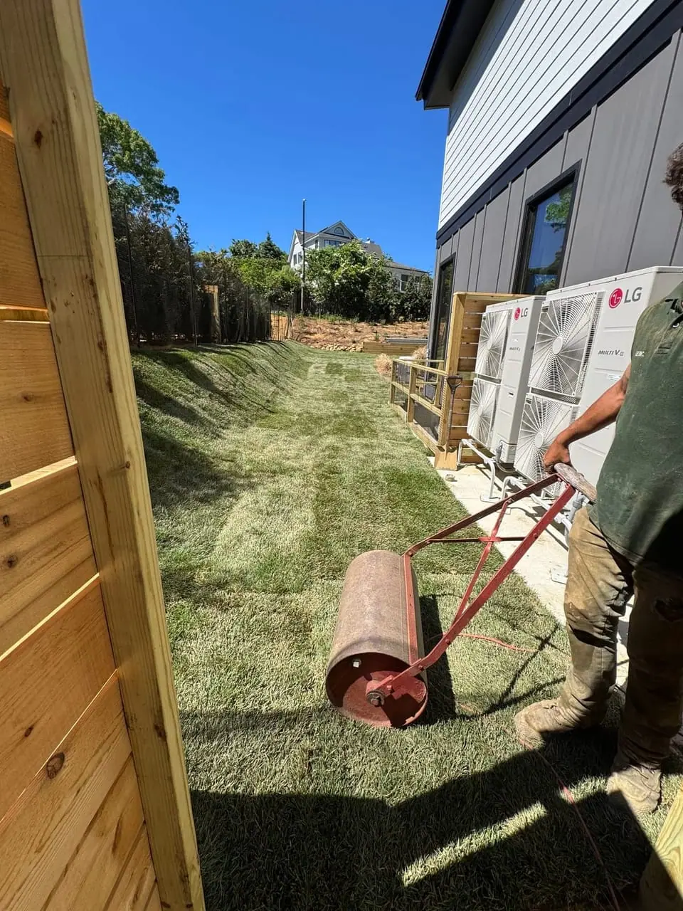 CT Sod installer using a lawn roller to press down freshly laid sod in the side yard during a sod installation in Montauk, NY