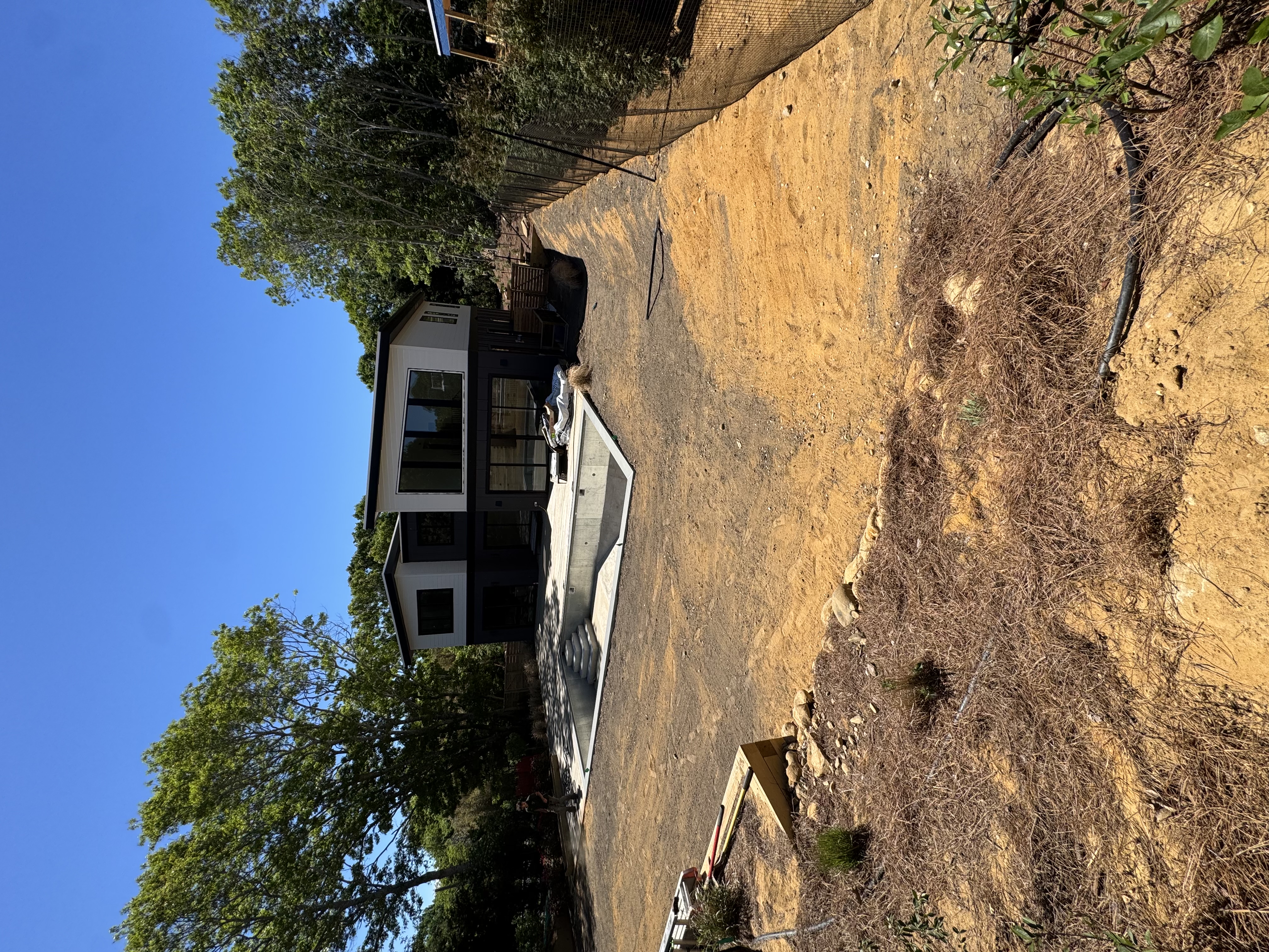 Graded dirt yard before sod installation at a Montauk, NY new-build home, with the pool and modern house behind the prepped soil