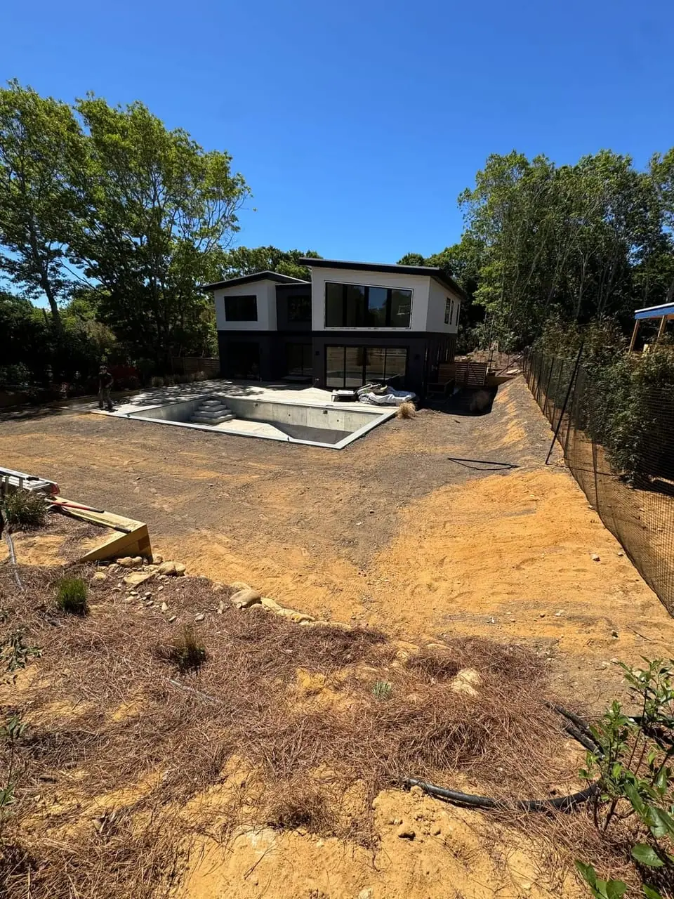 Graded dirt yard before sod installation at a Montauk, NY new-build home, with the pool and modern house behind the prepped soil