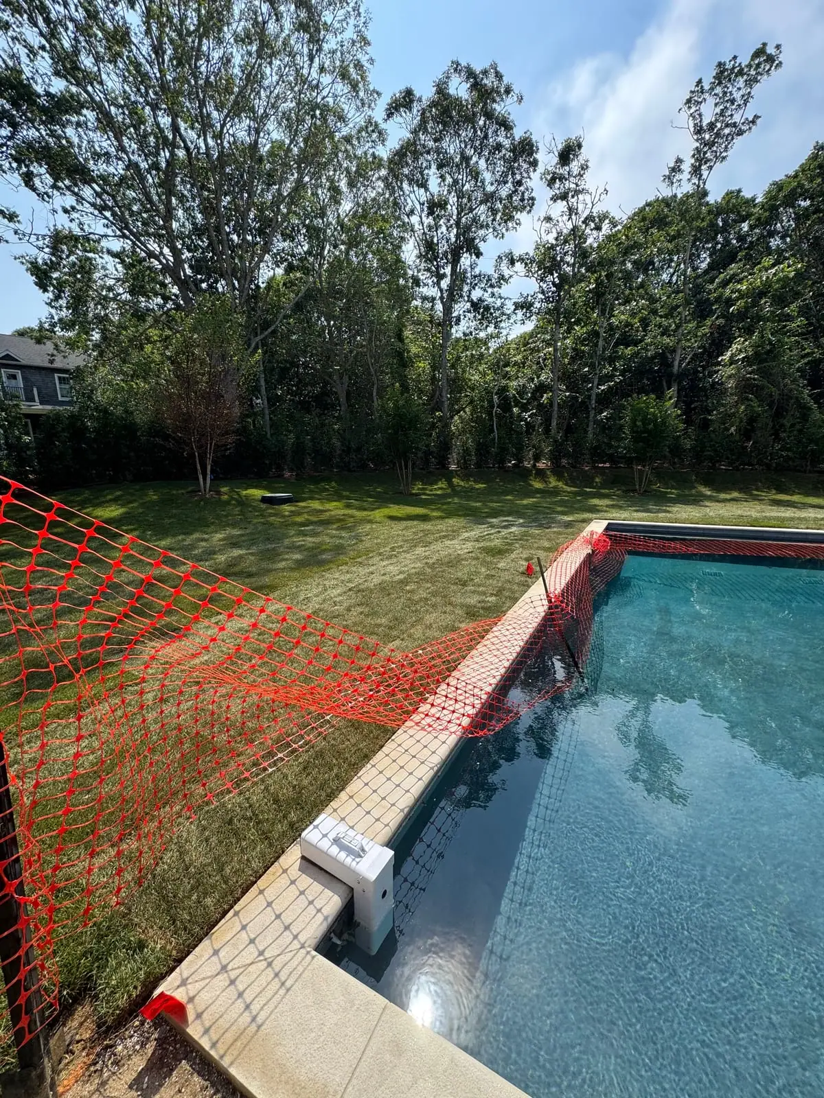 Elevated view over the pool-corner safety fencing across the full back lawn of freshly installed sod at the 4,500 sq ft Montauk, NY new build