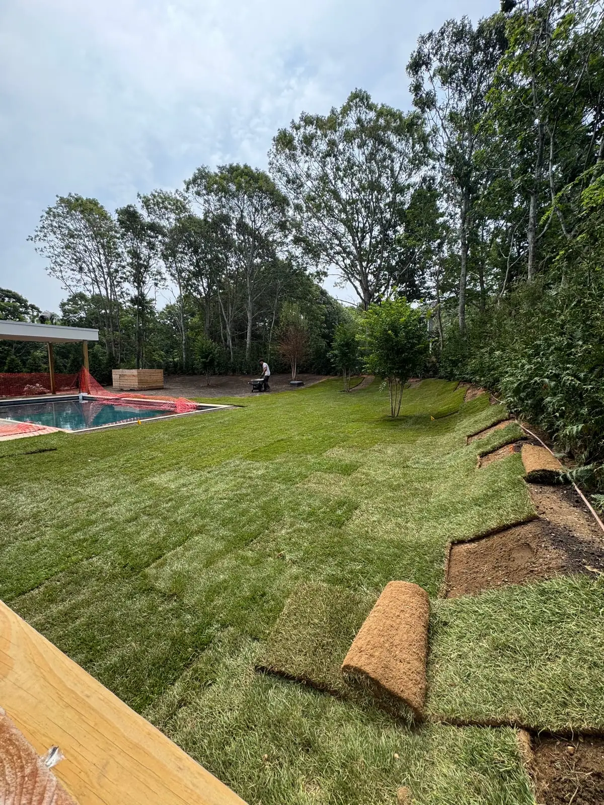 CT Sod crew laying fresh sod rolls up the back slope beside the pool at the Montauk, NY new build