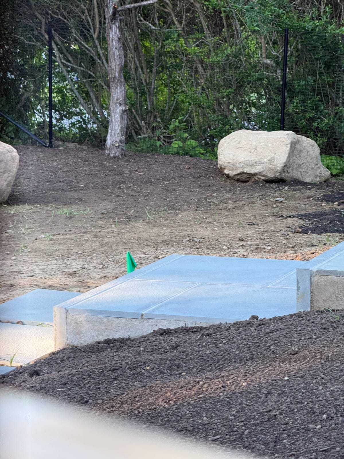 Bluestone patio landing, a set feature boulder, and black deer fencing framing the prepped grade off a new pool terrace in Montauk, NY