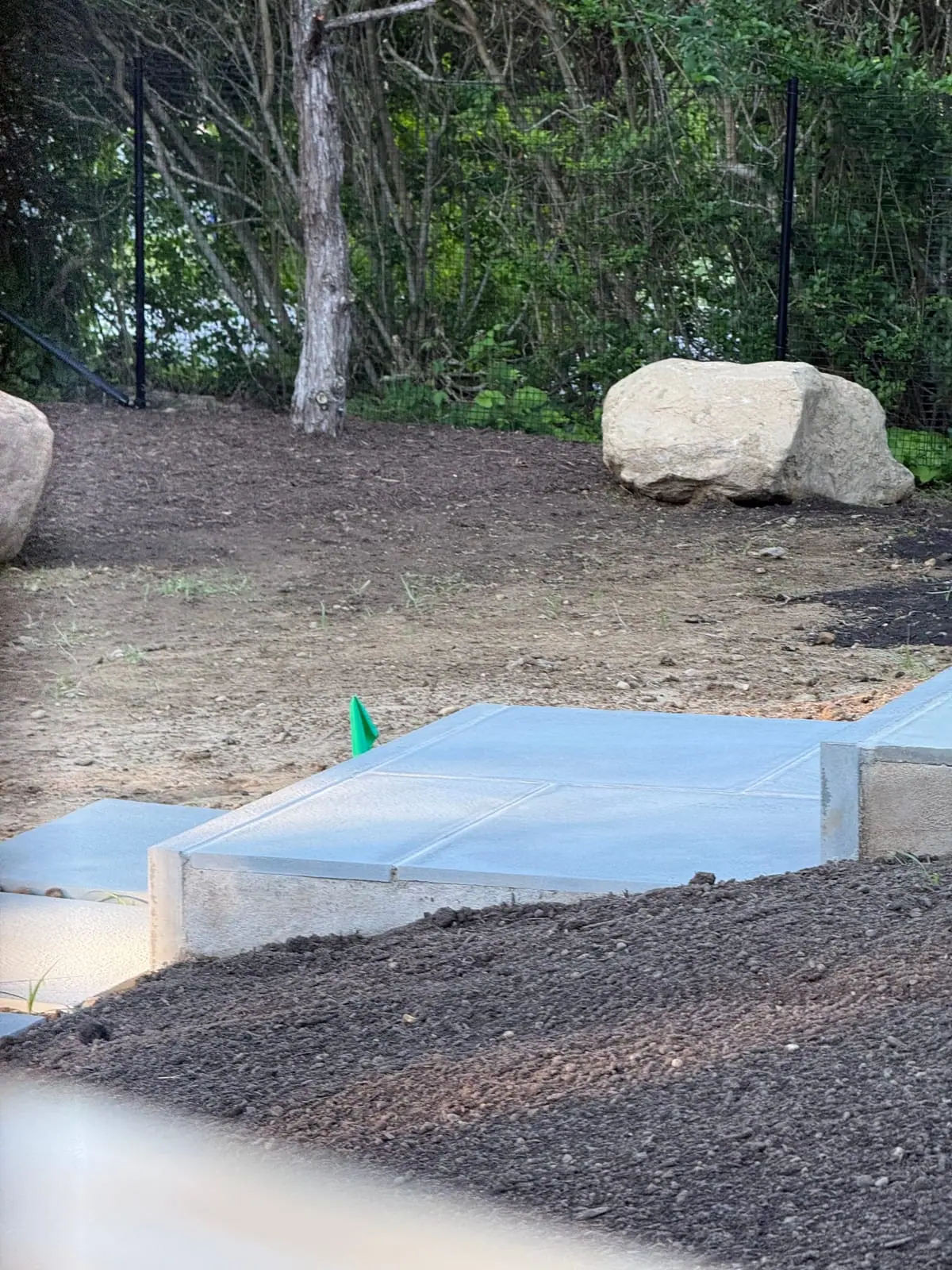 Bluestone patio landing, a set feature boulder, and black deer fencing framing the prepped grade off a new pool terrace in Montauk, NY