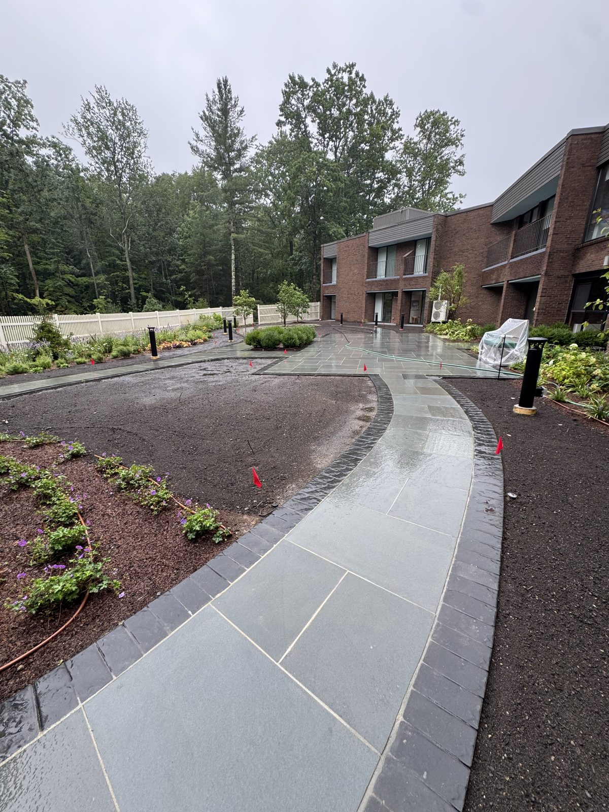 Wet bare soil around the curved bluestone walkway in the rain before sod installation in New Canaan, CT