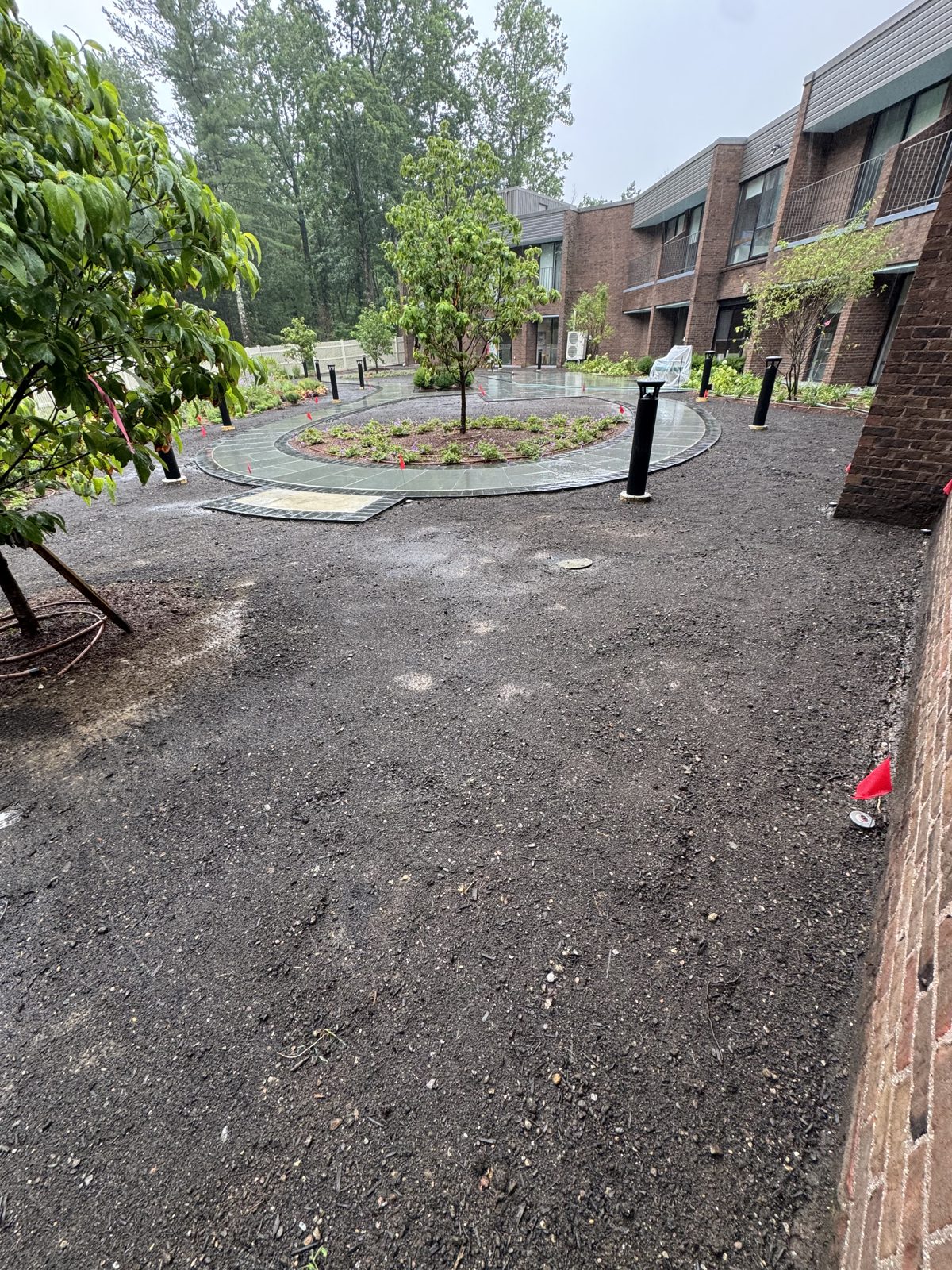 Bare graded soil in the rain beside a new bluestone patio and planting beds at a New Canaan, CT commercial property