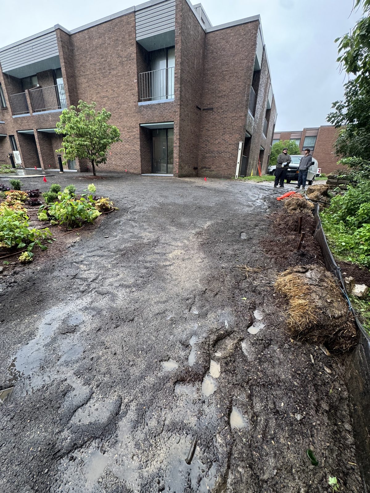 Muddy access path with standing water at a commercial property in New Canaan, CT, with two crew members and the delivery van in the rain