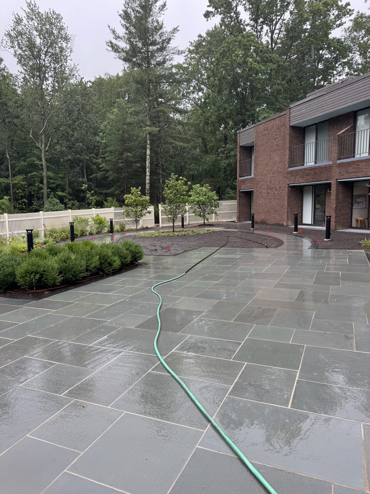 Rain-soaked patio and empty planting-bed areas before sod at a commercial property in New Canaan, CT