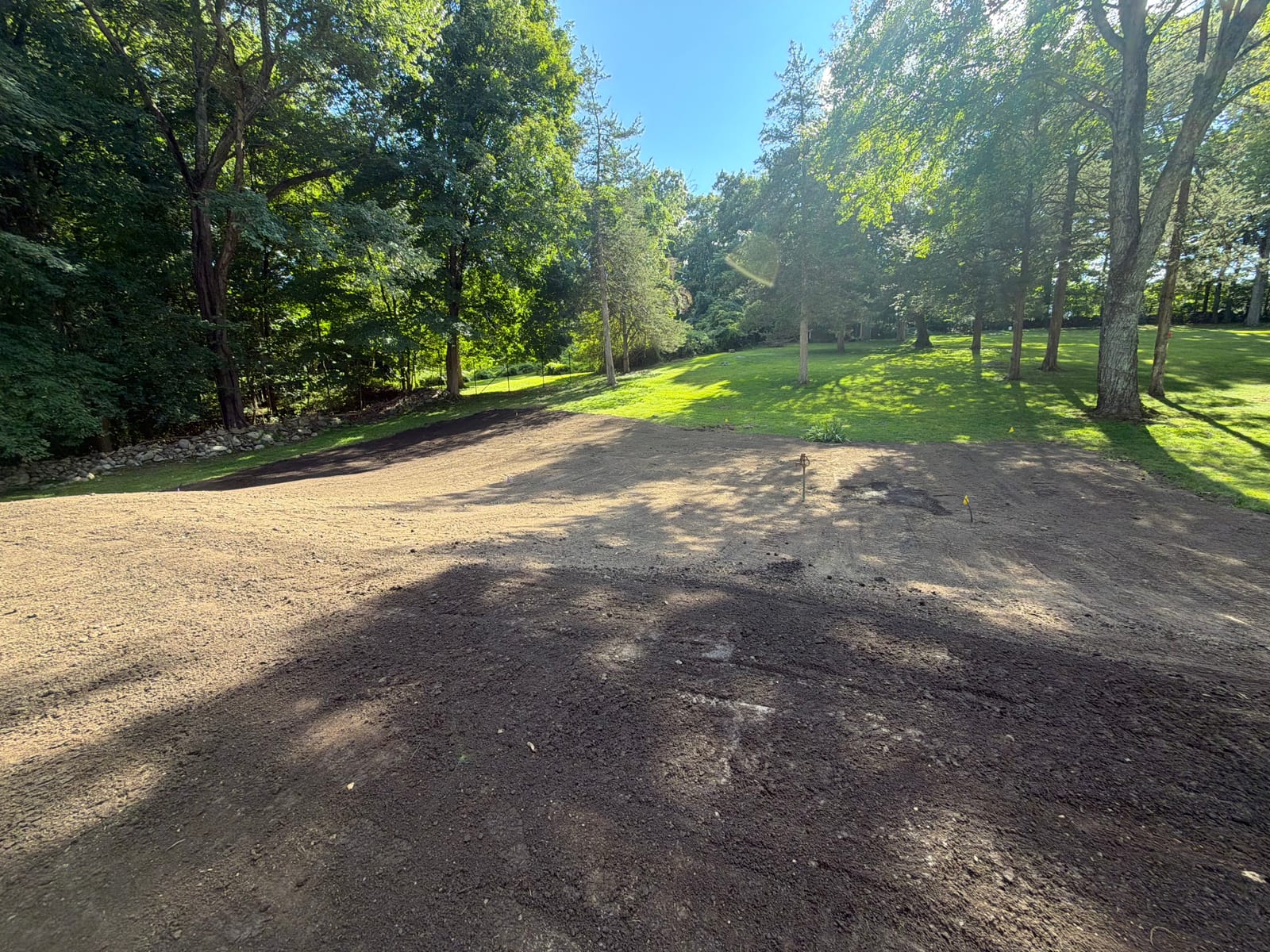 Finish-graded soil across the back lawn area at the New Canaan, CT sod project, meeting the established lawn at the tree line