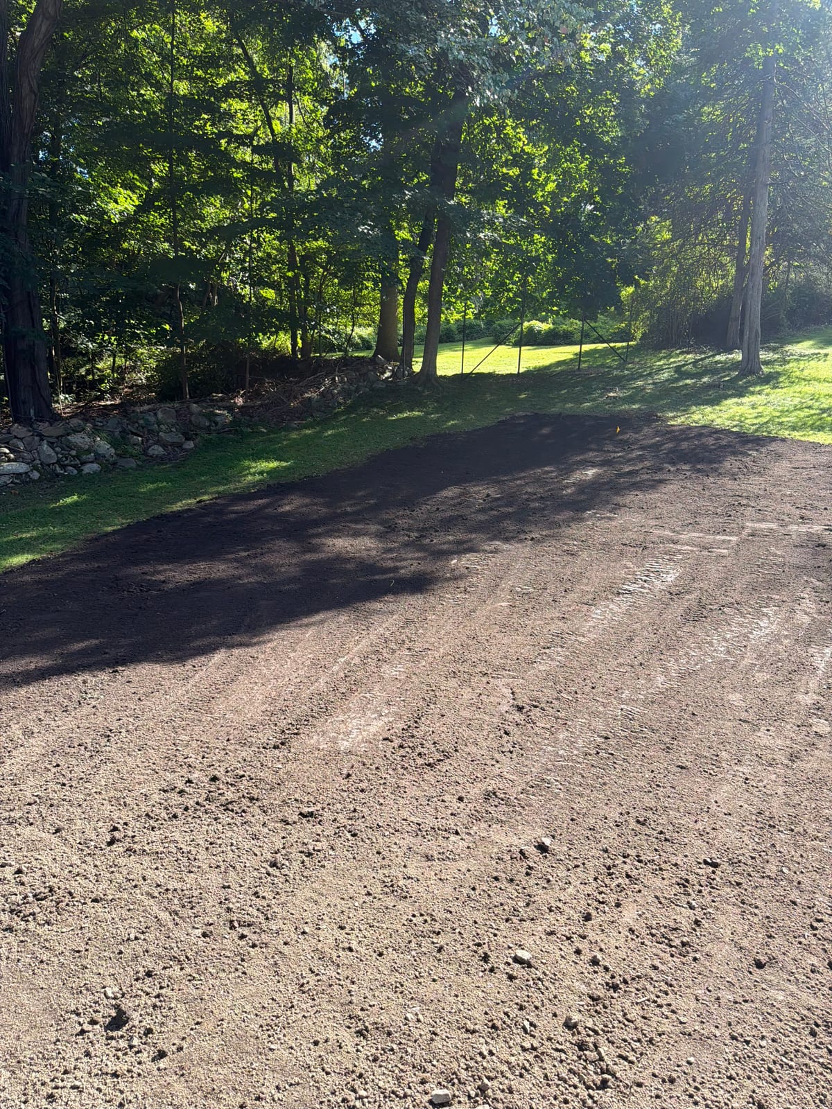 Finish-graded soil meeting the established lawn edge and stone wall at the New Canaan, CT sod project