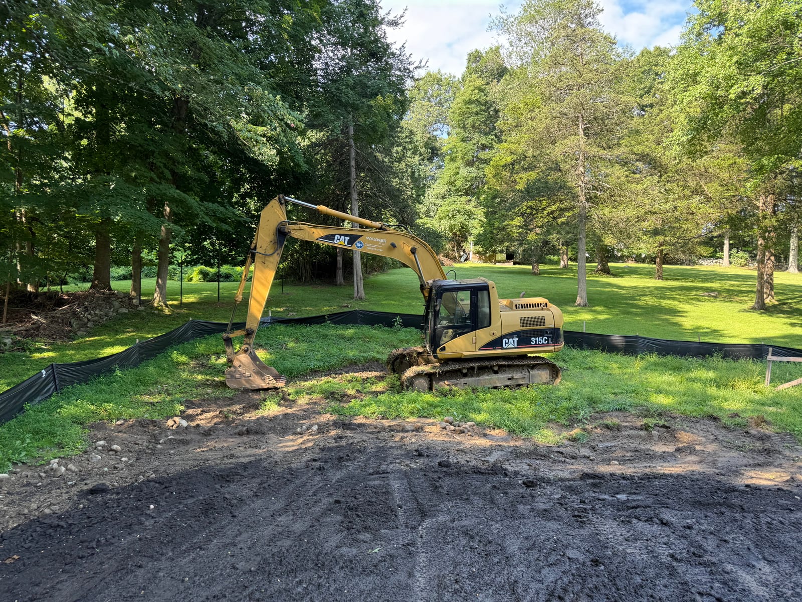 Excavator on dark graded soil along the silt-fence line at the New Canaan, CT sod project on Monday morning