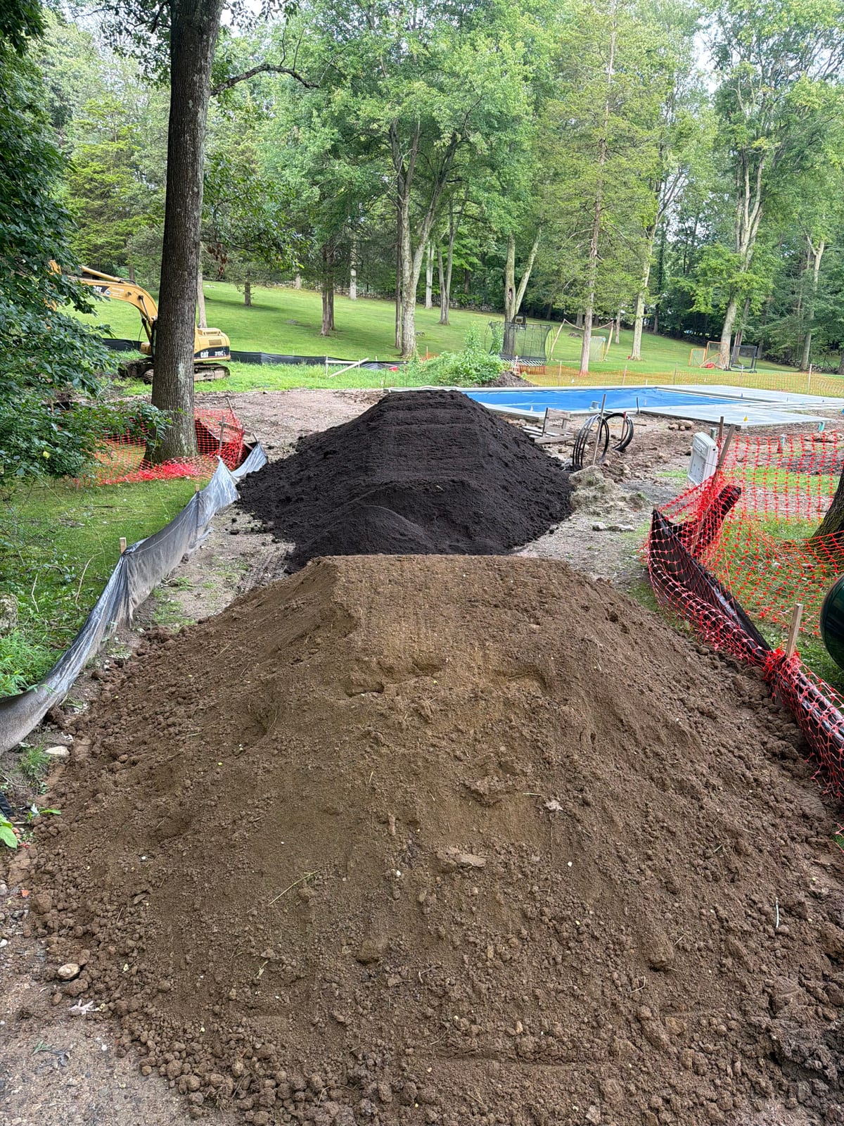 Tri-axle loads of screened fill and darker screened topsoil staged beside the covered pool at the New Canaan site on Saturday morning