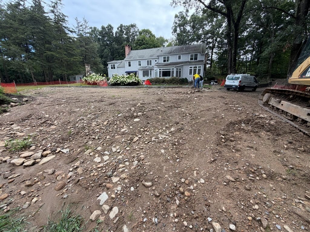 Rough residential yard in New Canaan before grading and sod installation, with the house and pool area beyond