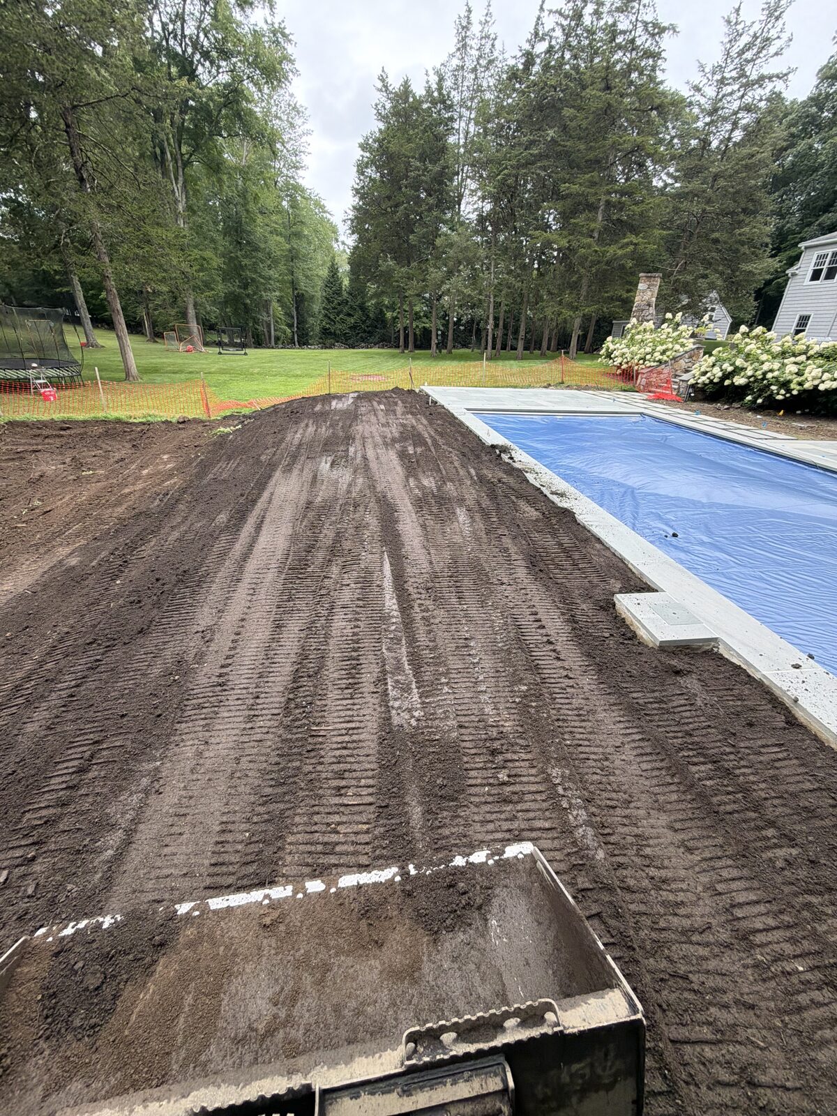 Freshly spread screened topsoil beside the covered pool at a New Canaan, CT property during full site preparation before sod installation