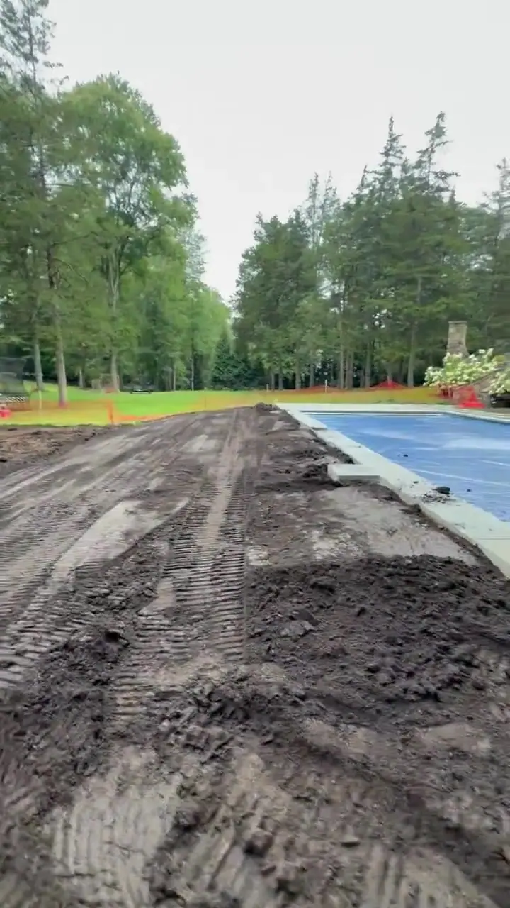A track loader works across the prepared New Canaan, CT lawn area beside the pool before sod installation