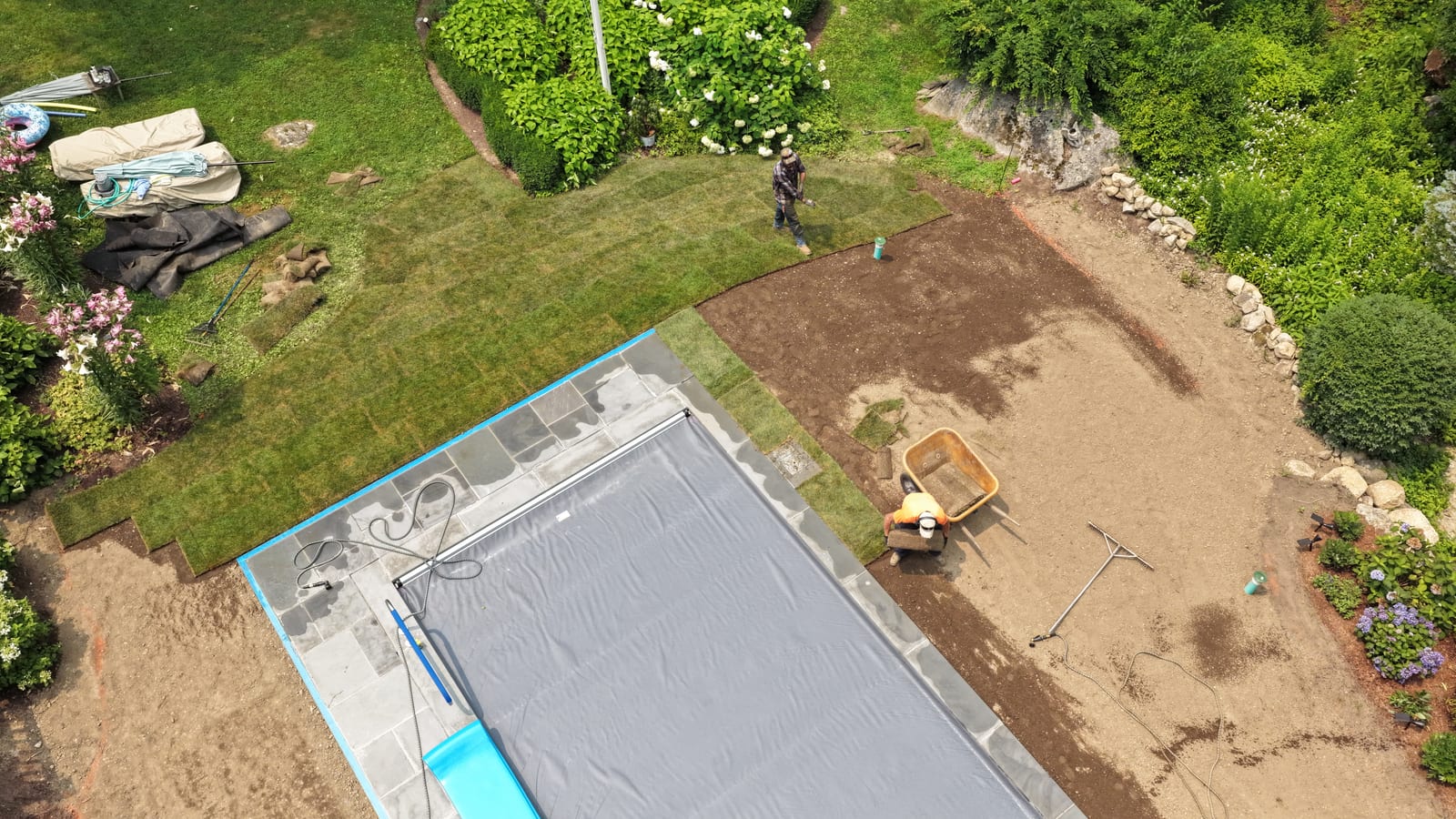Aerial view of the first sod rolls going down beside a covered pool at a New Canaan, CT installation