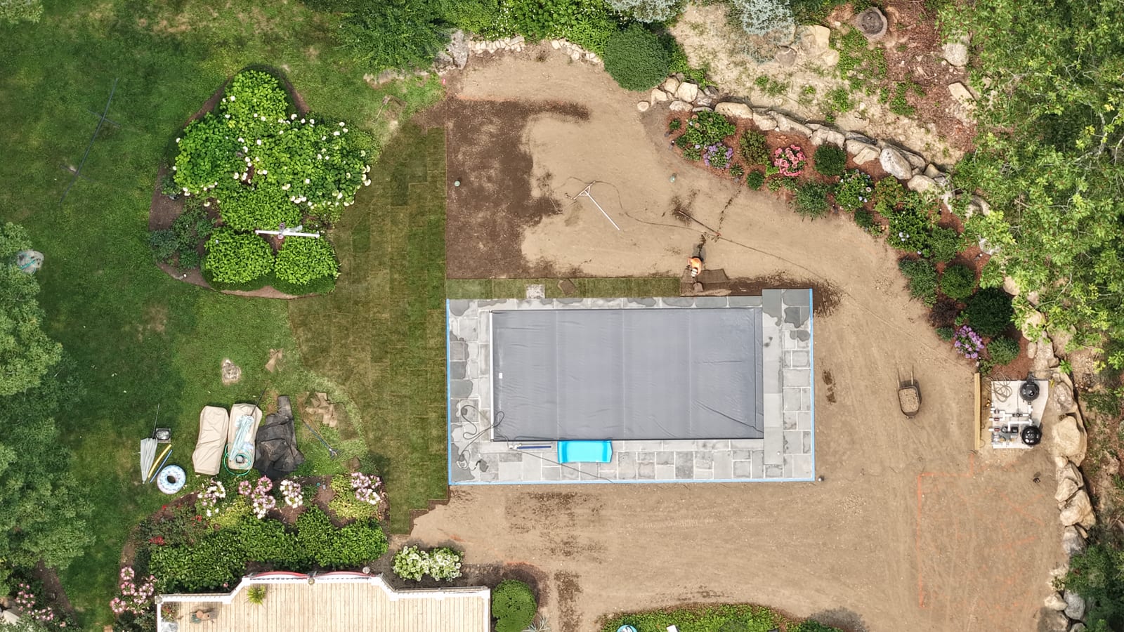 Straight-down drone view of a New Canaan, CT backyard during sod installation, with the first columns of fresh sod laid along the garden edge and the new covered pool centered in the graded yard
