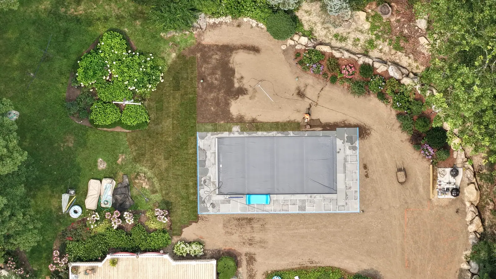 Straight-down drone view of the covered pool in New Canaan, CT with the first columns of fresh sod laid along the garden edge and the graded yard ready for the next rolls