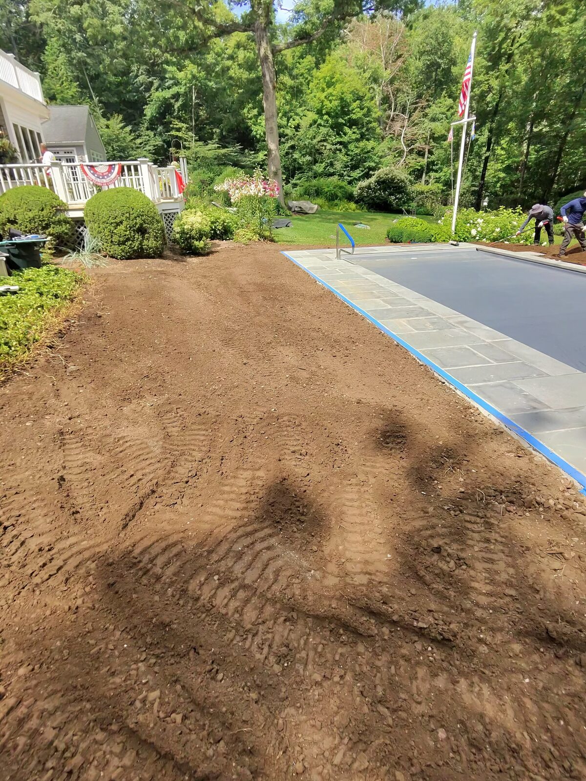 Our crew fine-raking the graded topsoil beside the new pool at a New Canaan, CT home, with the deck and established gardens untouched behind them