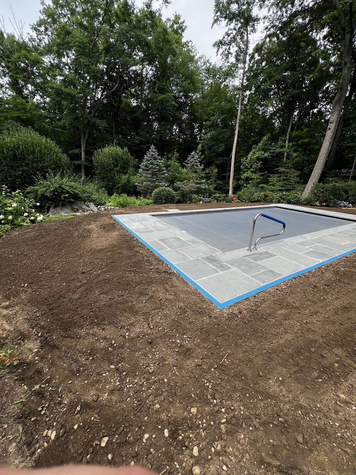 New stone coping and a stainless handrail on a covered pool in New Canaan, CT, with graded topsoil held just below the stone so the sod can finish flush