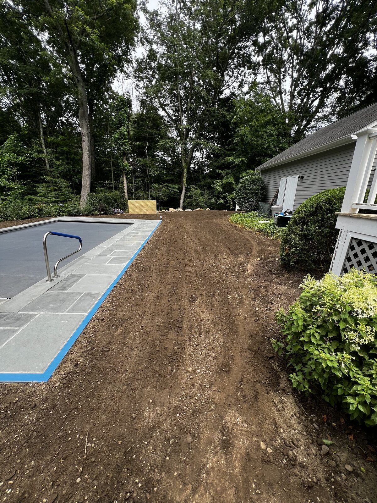 Graded topsoil running from the new pool past the house toward the back gardens in New Canaan, CT, edged clean along the plantings on both sides