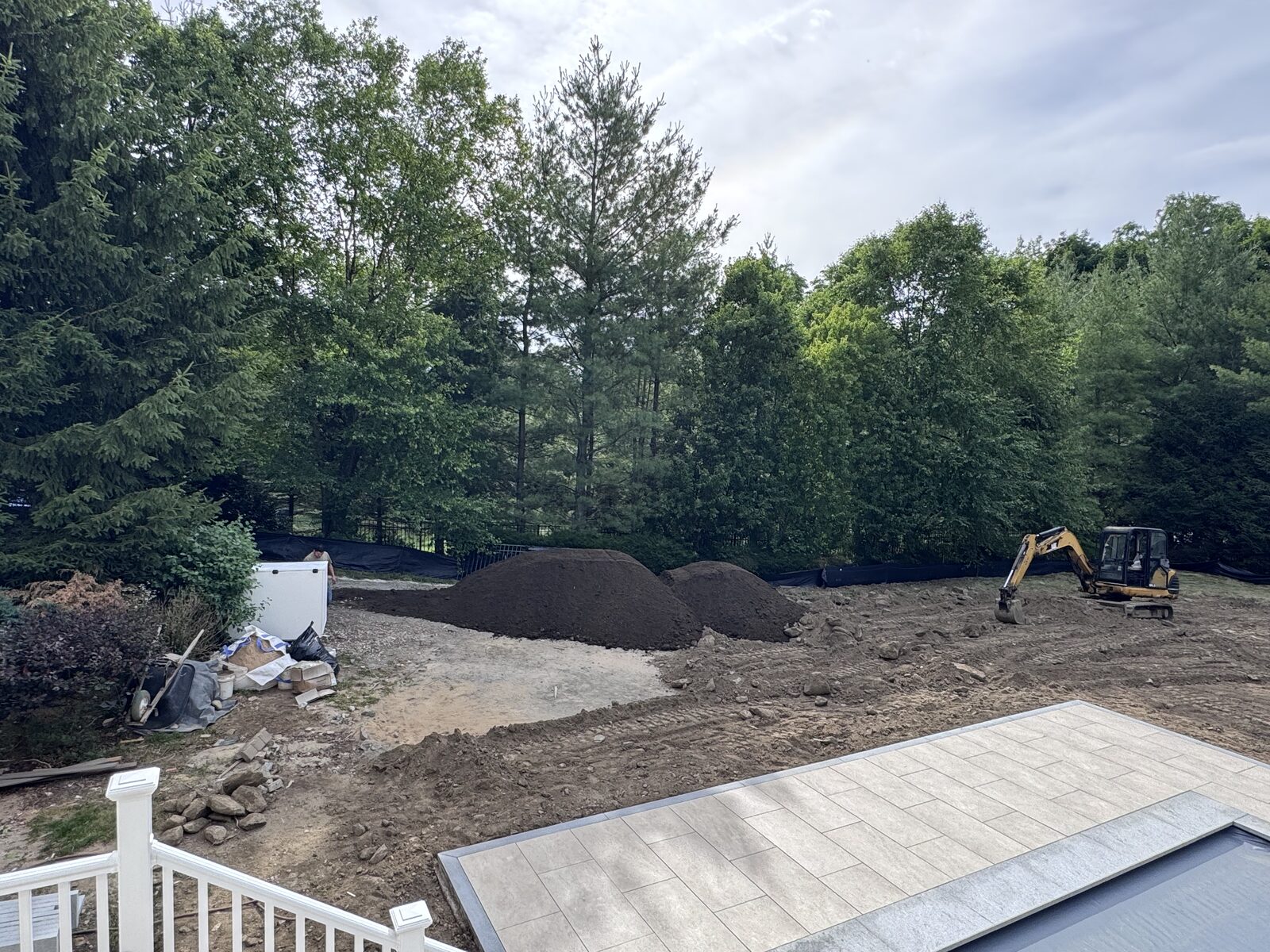 Excavator working beside piles of screened topsoil in a torn-up Purchase, NY backyard next to a new pool patio