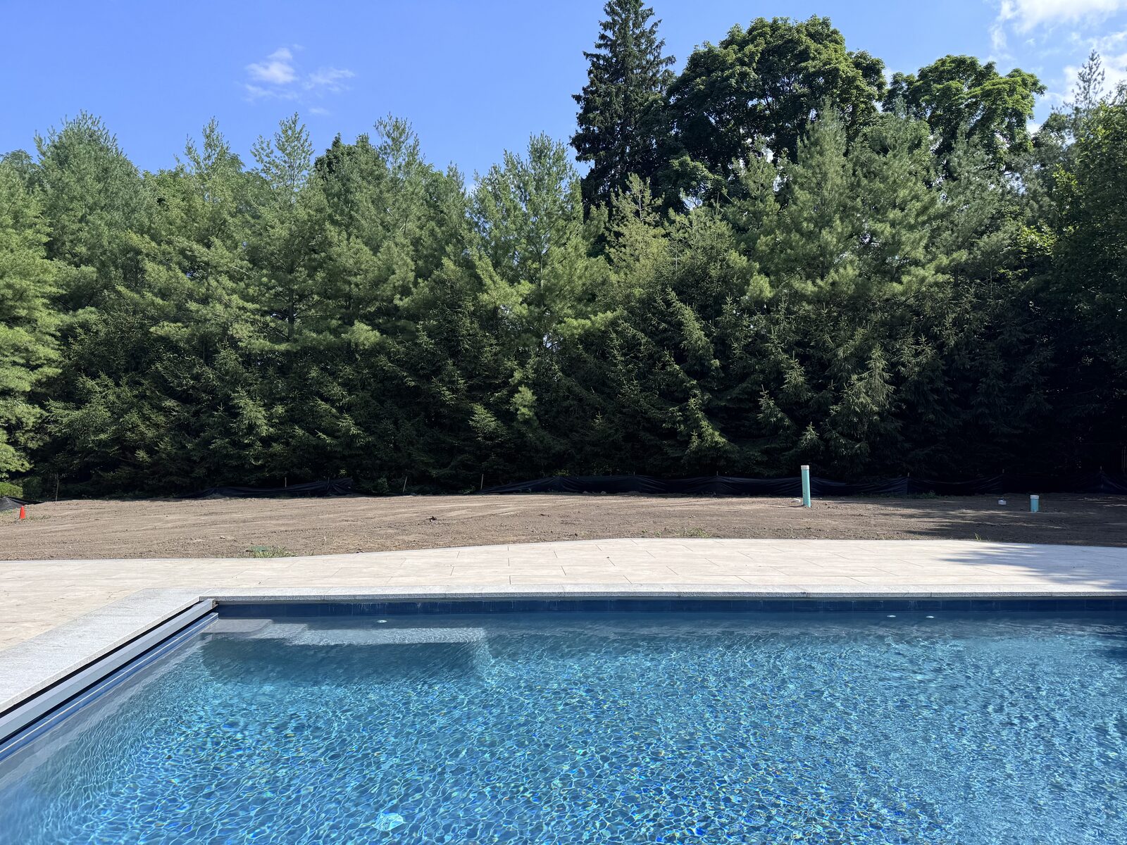New pool filled with water in Purchase, NY with the cleared and graded backyard behind it ready for sod installation