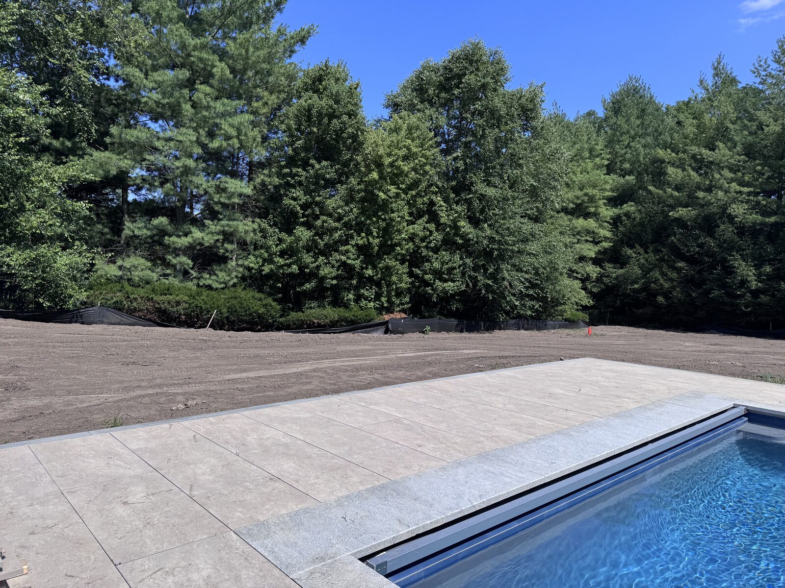 New swimming pool and stone patio in Purchase, NY surrounded by 12,000 square feet of graded bare dirt ready for sod installation