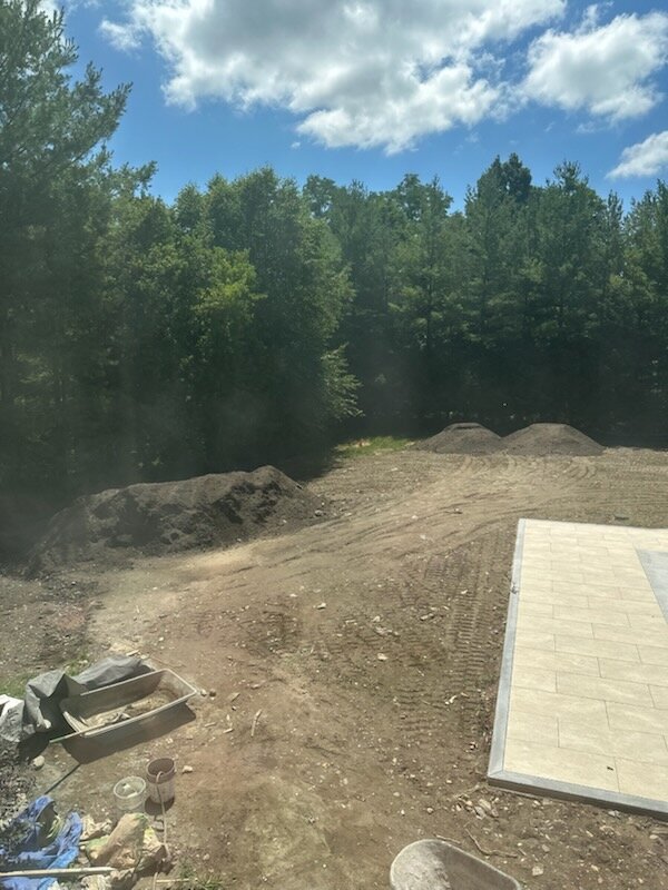 Piles of screened topsoil staged beside the new pool patio in Purchase, NY before final grading for sod