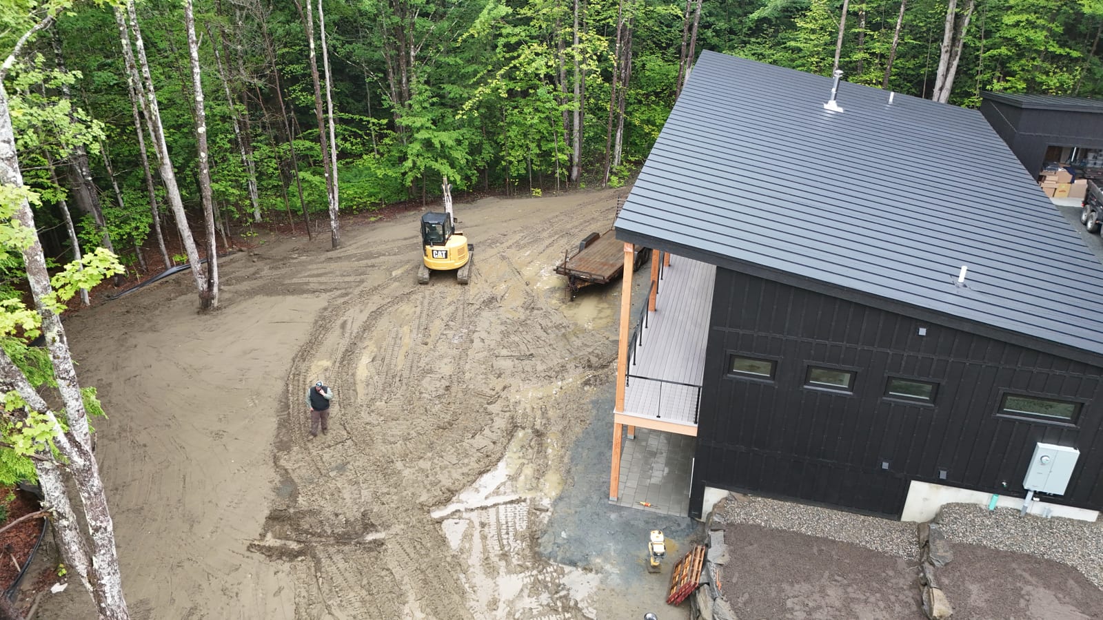 Aerial view of the muddy, rain-soaked sod site in Hartford, VT with an excavator parked in the churned ground