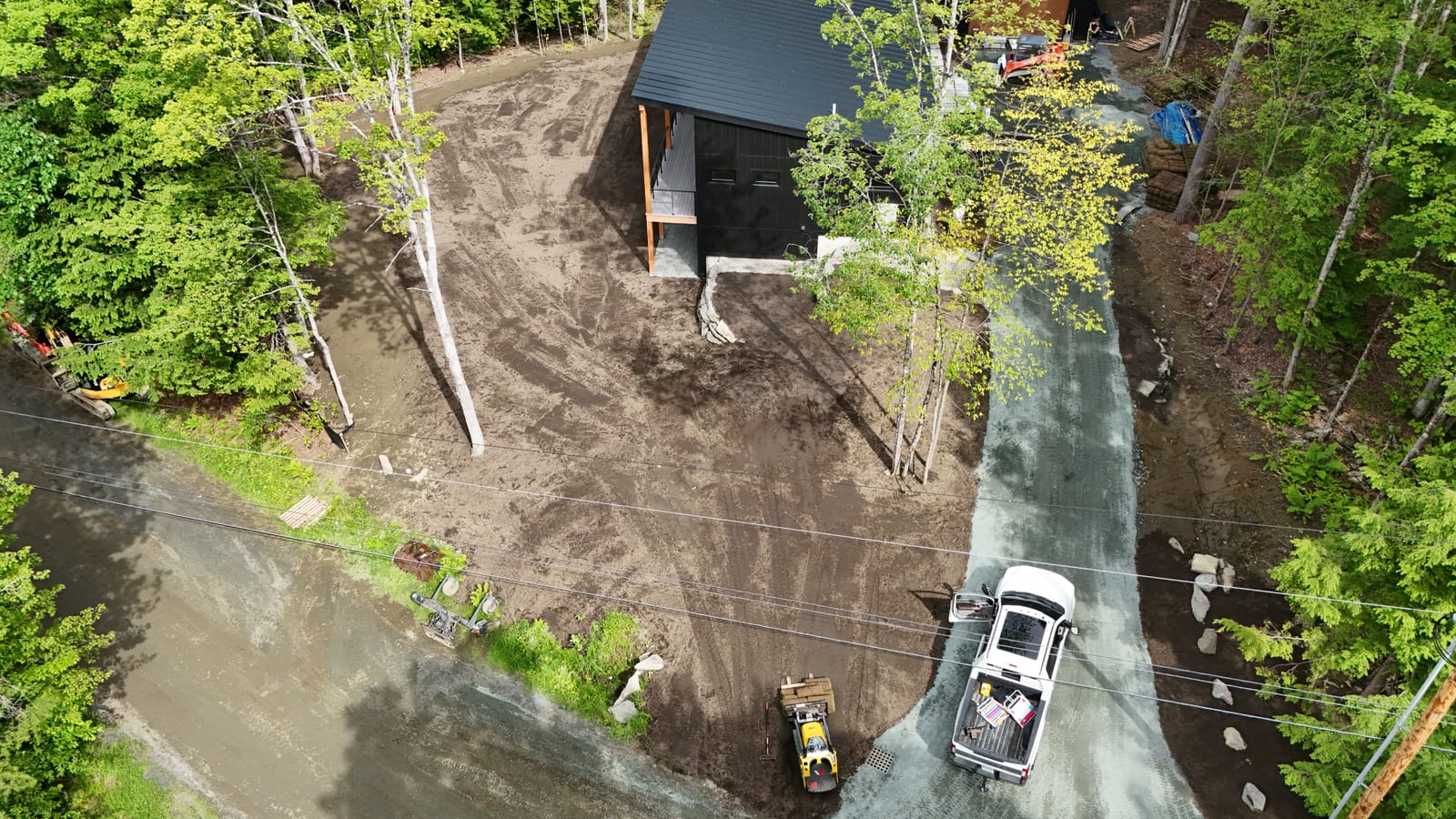 Top-down drone shot late in the day showing the full scope — the green lawn, the regraded pad, and the brand-new gravel driveway curving past the home