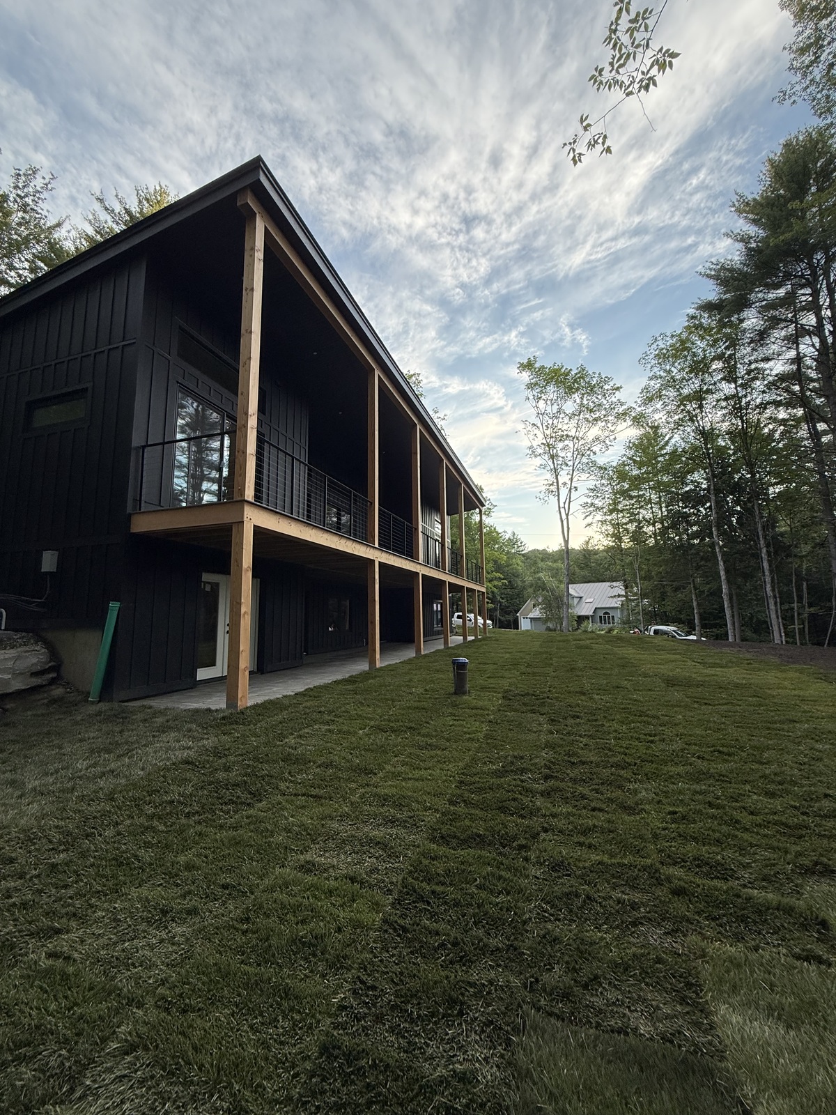 Wide evening view of the finished tall fescue sod lawn sweeping along the modern black home out to the Vermont tree line in Hartford (Quechee)