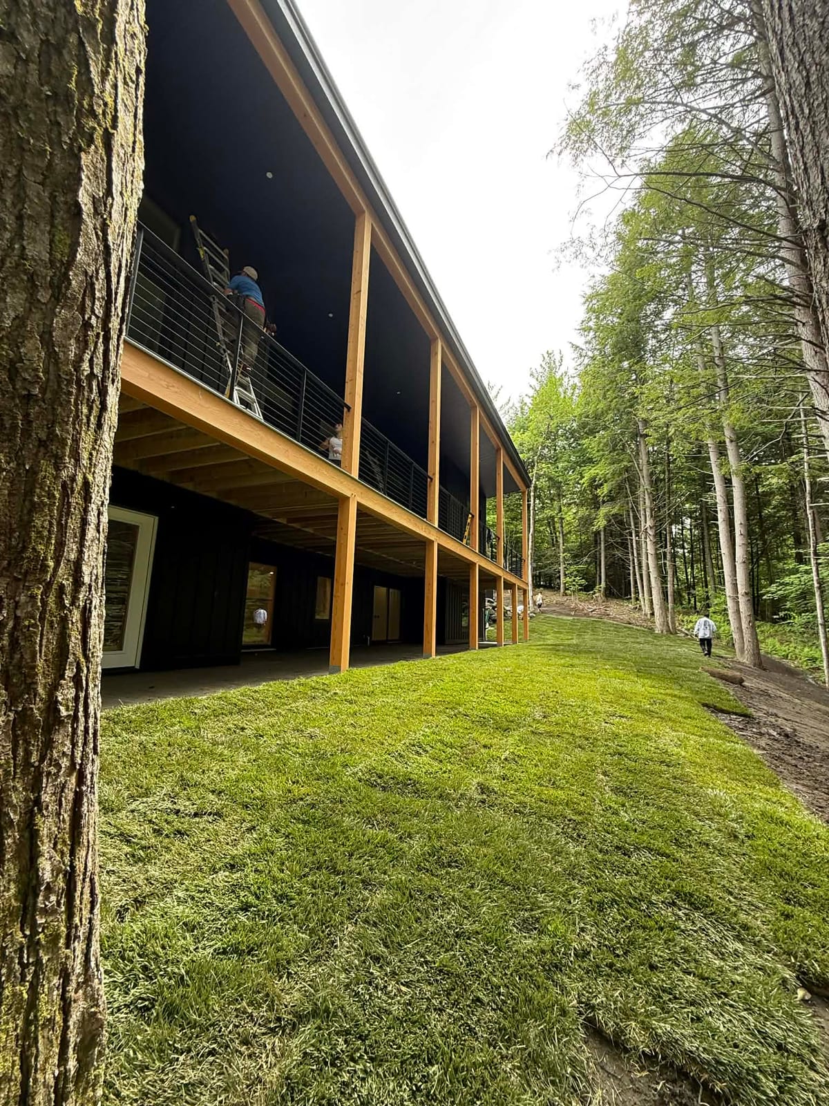 Lush finished tall fescue sod lawn running alongside the modern home's elevated deck in Hartford, VT, with the crew wrapping up