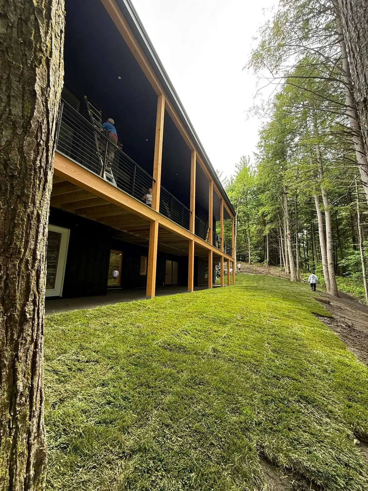 Lush finished tall fescue sod lawn running alongside the modern home's elevated deck in Hartford, VT, with the crew wrapping up