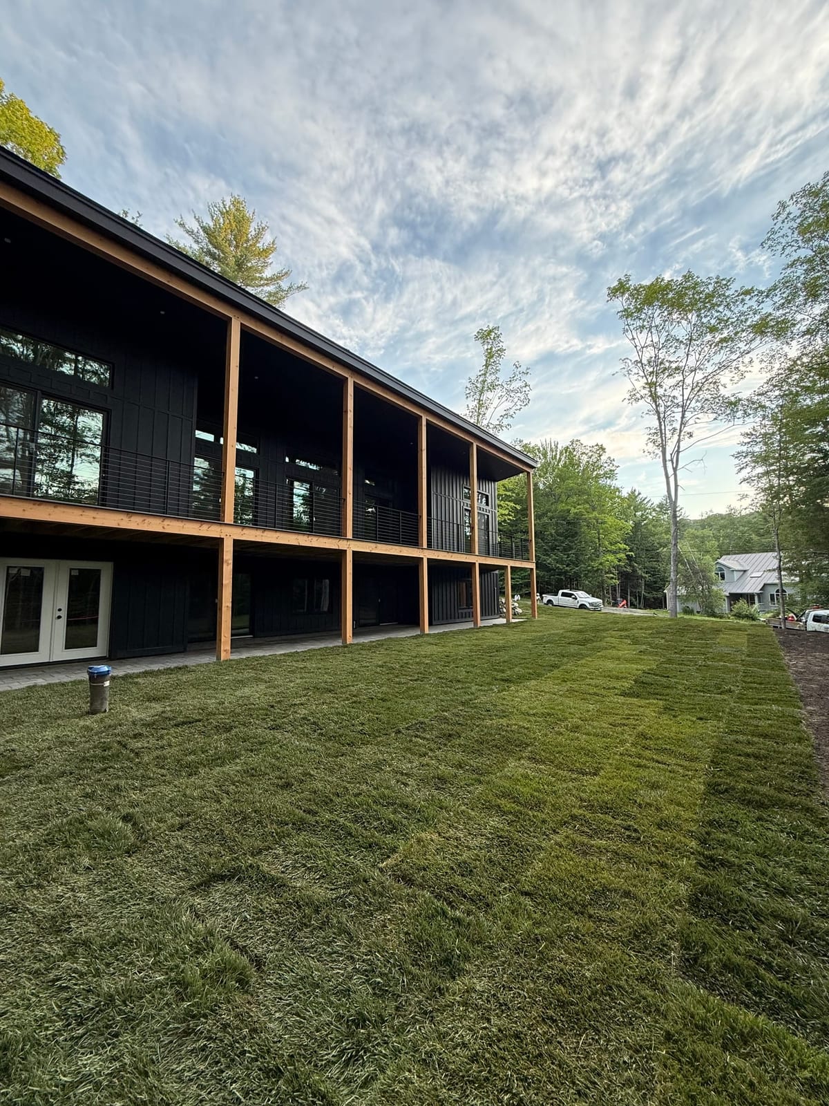 Newly laid tall fescue running tight along the side of the modern black home, seams knitted and edges cut clean to the foundation