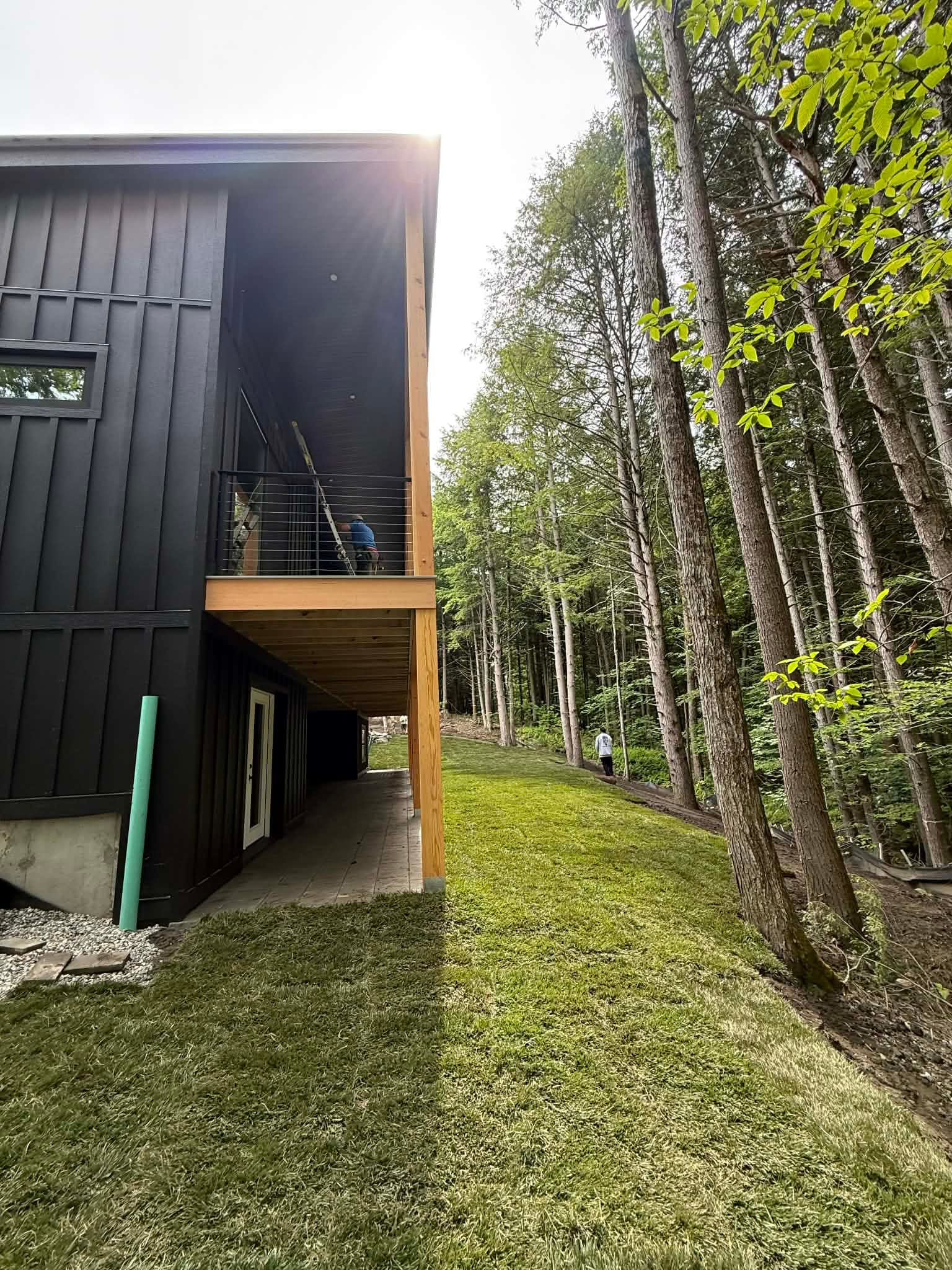 Evening sun flaring behind the modern home as the finished tall fescue lawn glows green along the cedar-post elevation in Quechee