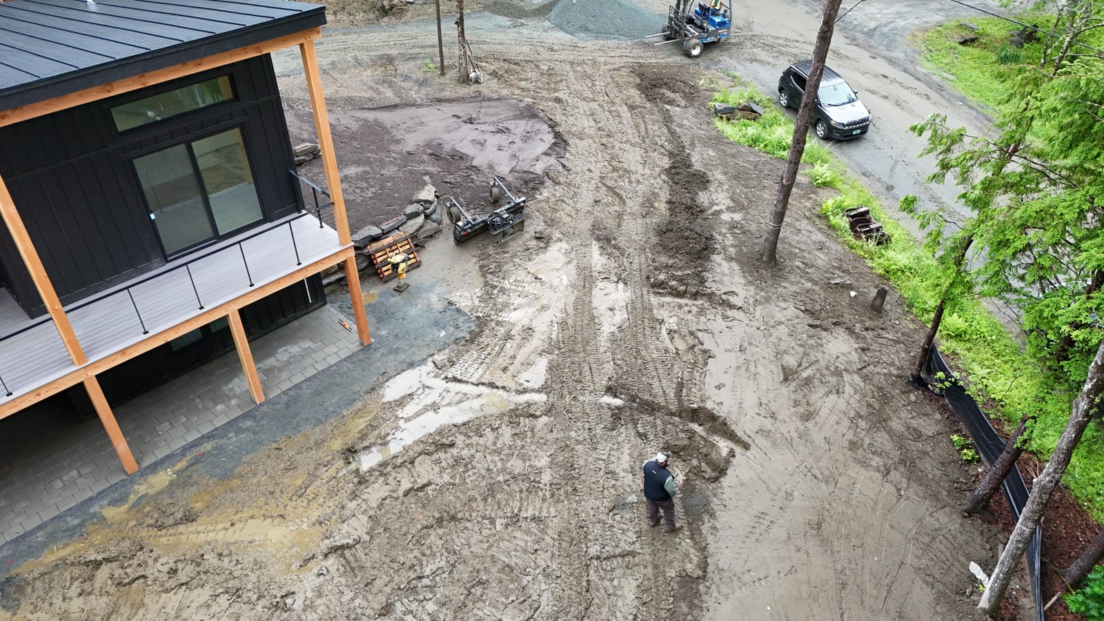 Drone view at 8:30 a.m. of a CT Sod worker raking the rain-soaked Quechee pad smooth, with fresh tall fescue pallets staged under the home's covered porch