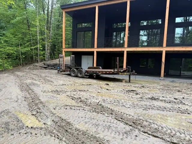 The Hartford, VT job site — a modern home with an equipment trailer parked on the rain-churned, muddy yard awaiting sod