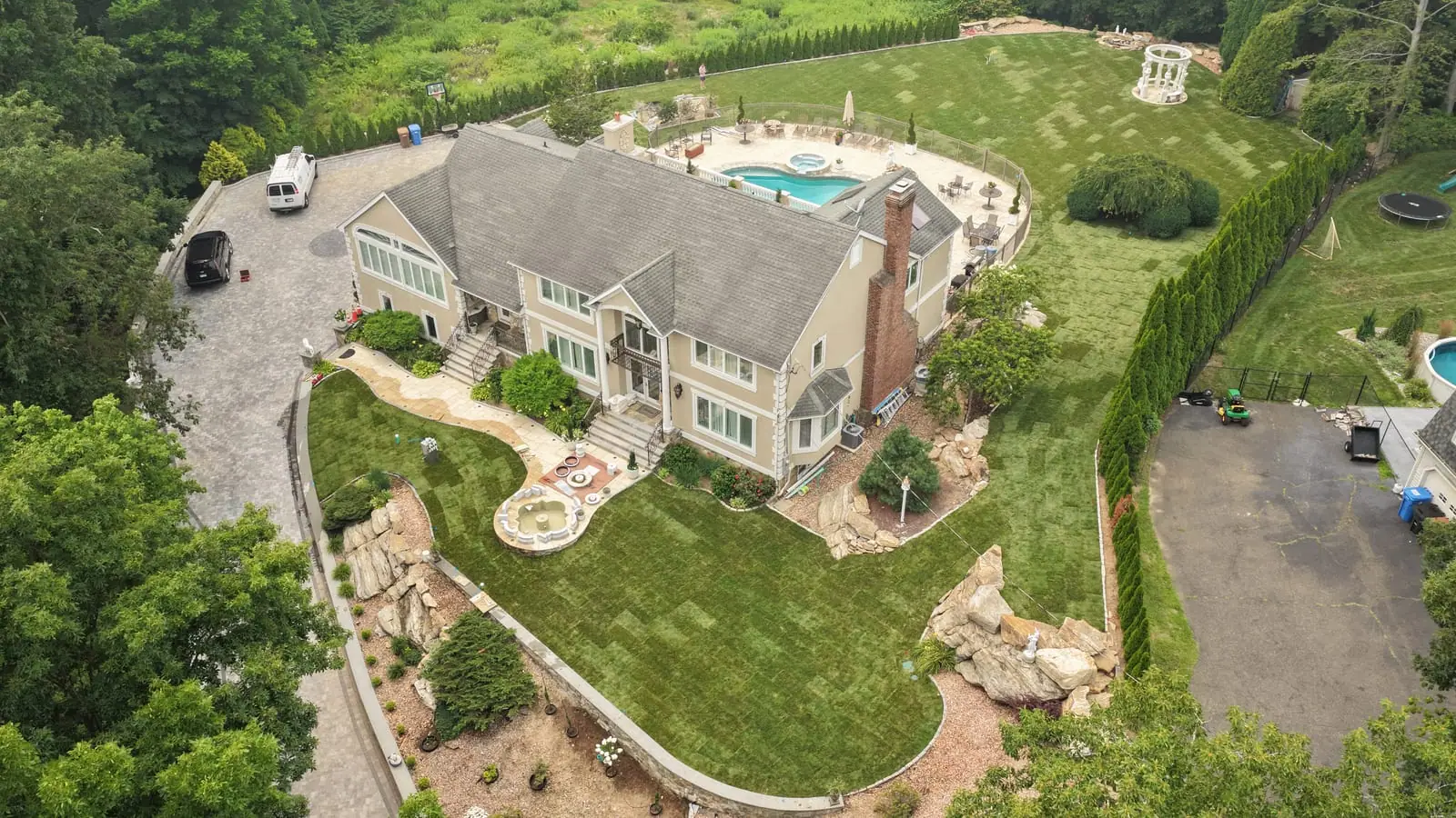 Aerial portrait of the Shelton, CT home after the sod installation — fresh sod wrapping the front fountain courtyard and side yards down to the stone ledges, pool and new lawn behind