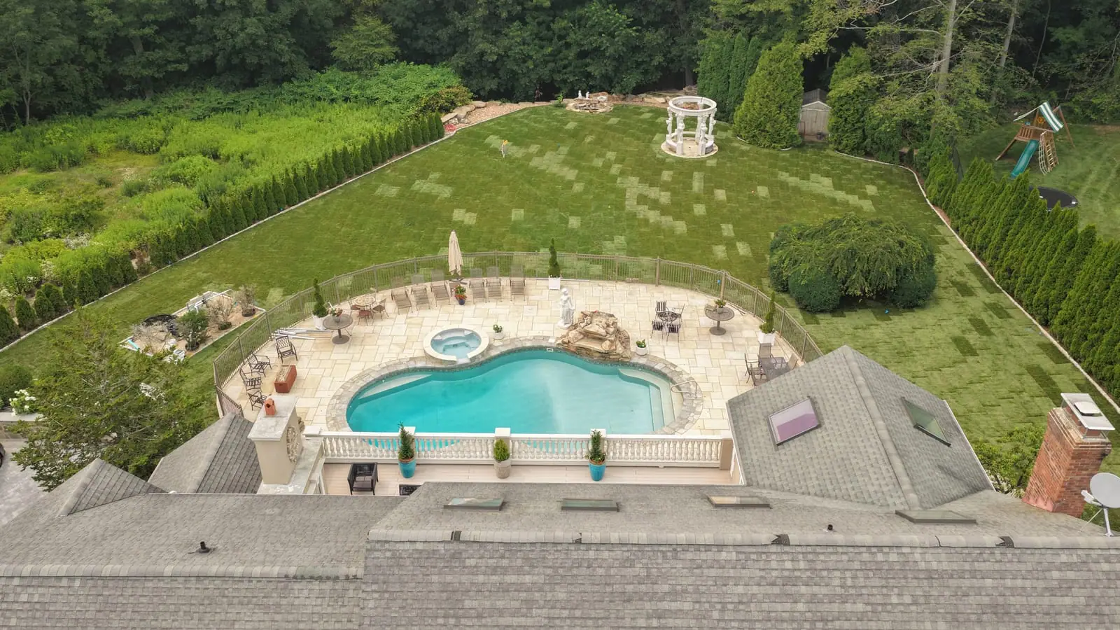 View over the roofline of the Shelton, CT home — new pool and spa patio below with fresh sod covering the backyard out to the gazebo and tree line